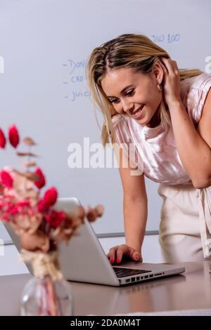 Une femme indépendante ravie assise à la table avec un ordinateur portable et travaillant à distance à la maison Banque D'Images