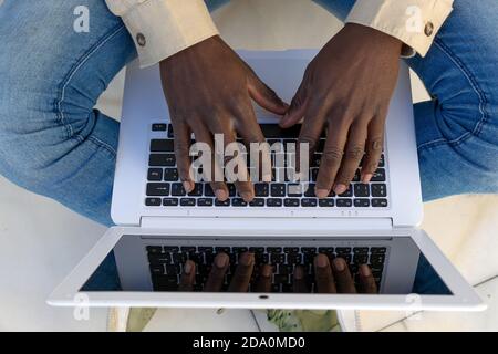 D'en haut, un homme noir non reconnaissable court assis dans la rue et la messagerie sur les réseaux sociaux via netbook tout en profitant du week-end Banque D'Images