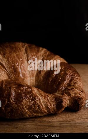 Gros plan sur un croissant croustillant appétissant placé sur une table en bois arrière-plan noir Banque D'Images