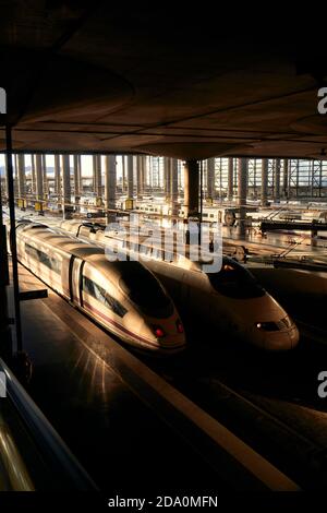 Des trains modernes circulent près de la plate-forme sous le toit de la gare sombre le soir en ville Banque D'Images