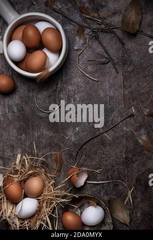 Vue de dessus des œufs de poulet entiers et fissurés de blanc et les couleurs brunes arrangées sur une surface désordonnée avec des plumes Banque D'Images