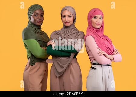 Trois musulmanes différentes Dames en hijab debout ensemble, fond jaune Banque D'Images