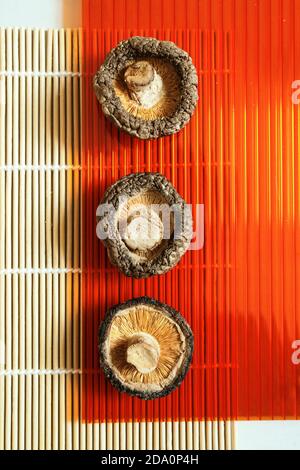 Vue de dessus des appétissants champignons shiitake secs disposés en rangée sur un tapis en bambou sur la table Banque D'Images