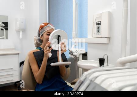 Patiente assise sur une chaise et regardant le miroir après recevoir des soins dentaires de dentistes professionnels en clinique moderne Banque D'Images