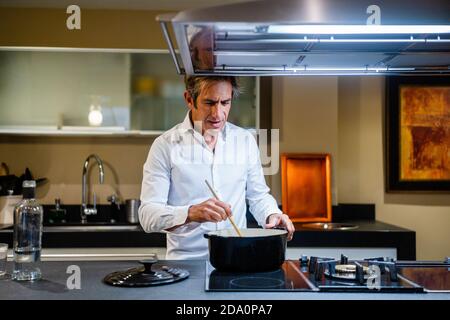 Dîner de cuisine gaie de l'homme d'âge moyen dans la cuisine moderne avec lampe brillante Banque D'Images
