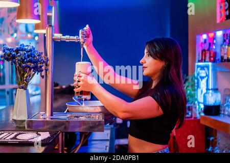 Vue latérale d'une jeune femme de service qui verse de la bière dans un verre tout en travaillant dans la barre Banque D'Images