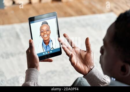 Vue sur l'épaule d'un patient africain, appel vidéo médecin virtuel sur une tablette. Banque D'Images