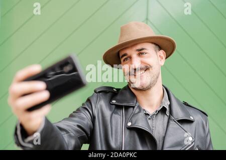 Gai heureux barbu galant mâle dans le chapeau prenant la photo dans cour de porte verte Banque D'Images