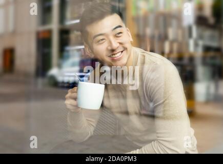 Homme asiatique se détendant dans un fauteuil dans un café confortable et dégustez une boisson chaude tout en regardant loin Banque D'Images