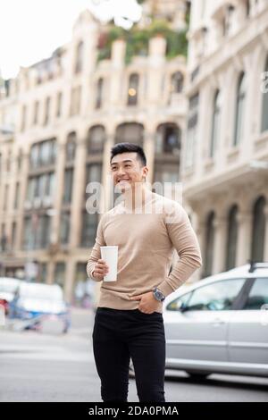 Homme asiatique gai debout près du bâtiment avec un cocktail sucré à profitez d'un week-end en ville tout en admirant la vue Banque D'Images