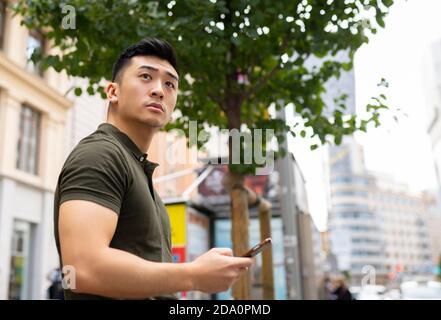 Vue latérale angle bas de grave asiatique homme de navigation de téléphone portable en ville et en plein air Banque D'Images