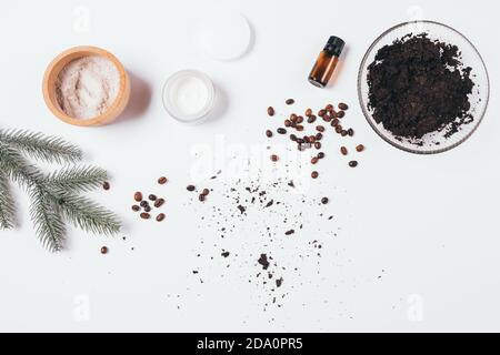 Ingrédients pour le gommage au café maison avec de l'argile et de l'huile essentielle de pin à côté de l'hydratant et de la branche d'épinette sur la table blanche, vue de dessus. Banque D'Images