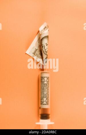 Du dessus de la seringue médicale en plastique avec roulé un dollar bill et le billet de banque yuan placés sur fond orange démontrant la devise échange concep Banque D'Images
