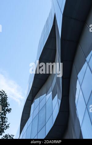 De dessous de bâtiment futuriste avec extérieur en forme de vague fait de panneaux de verre situés contre le ciel bleu dans le centre-ville Banque D'Images