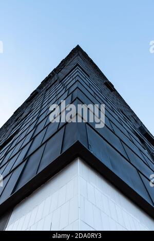 De dessous de l'angle de bâtiment géométrique contemporain avec noir extérieur en ville sur fond de ciel bleu sans nuages Banque D'Images