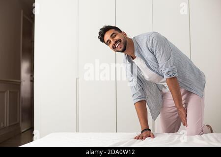 Homme gai portant des vêtements de maison faisant doux lit dans confortable chambre après réveil le matin Banque D'Images