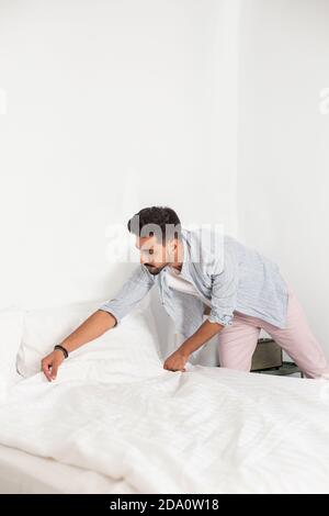 Homme calme portant des vêtements domestiques faisant un lit doux dans confortable chambre après réveil le matin Banque D'Images