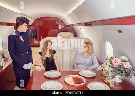 Une hôtesse d'air dessert les passagers de la classe affaires à l'intérieur de l'avion. Banque D'Images