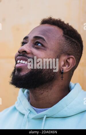 Joyeux adulte afro-américain hipster homme portant le pull à capuche bleu rire en vous tenant contre le mur jaune de la rue Banque D'Images