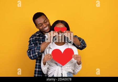 Un jeune homme afro-américain heureux met le cœur aux yeux des femmes, la dame tient le cœur Banque D'Images