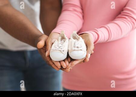 Gros plan des chaussures de bébé dans les mains de couple noir enceintes Banque D'Images