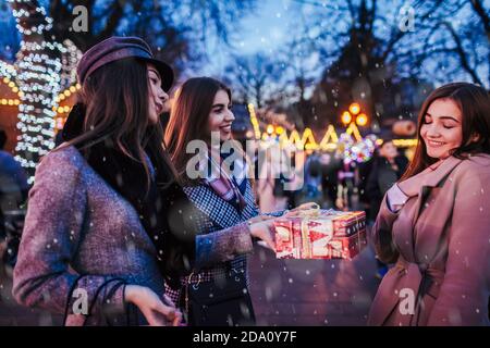 Nouvel an, cadeaux de Noël. Les amies donnent une boîte cadeau à leur amie en plein air. Célébration des vacances d'hiver Banque D'Images