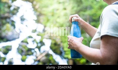 Vue latérale courte d'une femme voyageur méconnaissable avec sac à dos debout sur la pente avec une bouteille d'eau potable tout en admirant le paysage étonnant de la rade Banque D'Images