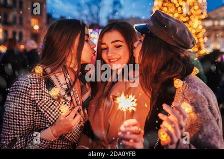 Nouvelle année. Femmes amis brûlant des spameurs à Lviv par arbre de Noël sur la rue salon embrassant sur la joue ayant le plaisir Banque D'Images