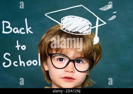 Mignon petit garçon d'âge préscolaire dans une salle de classe. Fond de tableau noir. Journée des enseignants. Enfants de l'école primaire. 1er septembre - salle de classe. Banque D'Images