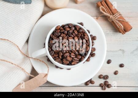 Tasse à café en grains, chandail et cannelle sur fond de bois blanc. Banque D'Images