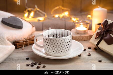 Une tasse sur une soucoupe, pas complètement rempli de grains de café sur un fond en bois avec des lumières allumées en arrière-plan. Banque D'Images