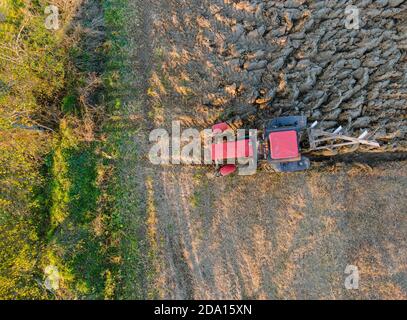 Vue aérienne du tracteur rouge labourant le champ en automne dans la soirée au coucher du soleil. Banque D'Images