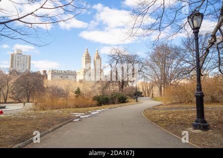 Central Park, New York City, mars 2019, chemin sinueux. Le sol est encore partiellement gelé avec de la glace. Le bâtiment San Remo est visible au centre. Banque D'Images