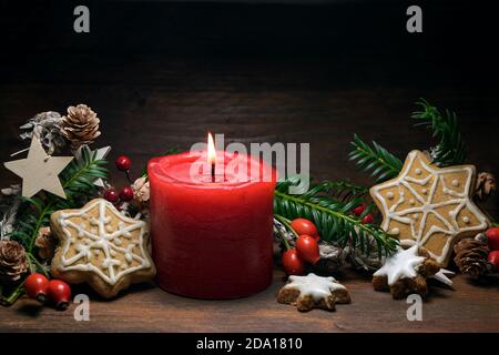 Décoration de Noël avec une bougie rouge, des biscuits au pain d'épice, des hanches roses, des branches et des cônes sur un fond de bois rustique foncé, espace de copie, sel Banque D'Images