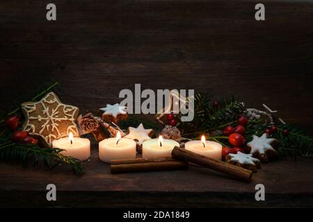 Quatre petites bougies allumées pour l'Avent et la décoration de Noël comme des biscuits de pain d'épice, des branches et des hanches roses sur un fond de bois rustique foncé, genero Banque D'Images