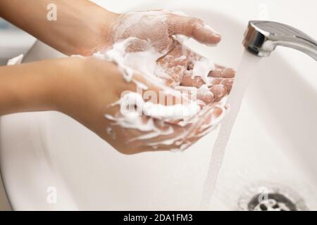 Enfant se laver les mains avec du savon et de la mousse copieuse sous l'eau courante dans la salle de bains au-dessus d'un lavabo blanc et d'un robinet chromé. Le concept de pureté de Banque D'Images