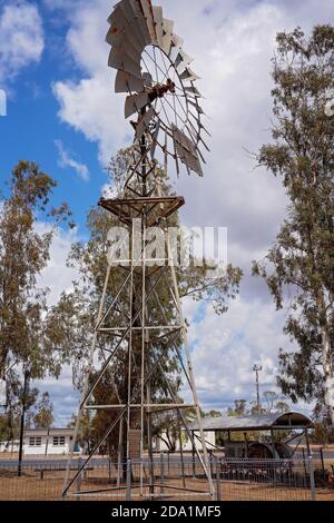 Warra, Queensland, Australie - octobre 2019 : moulin à vent qui pompe de l'eau parmi les arbres et contre un ciel bleu nuageux Banque D'Images