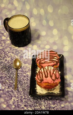 Deux beignets en glaçage rose et une tasse de cappuccino sur fond gris brillant. Gros plan. Banque D'Images