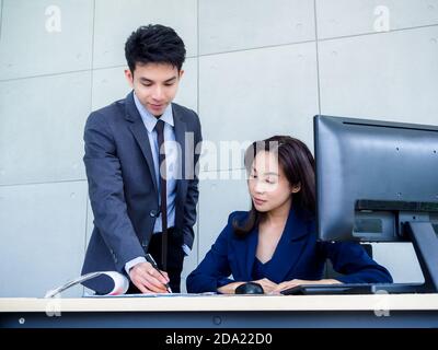 Femme d'affaires asiatique et homme d'affaires vêtu d'un costume travaillant ensemble au bureau. Jeune employé de sexe masculin se tenant sur la carte pour consulter des emplois avec fem Banque D'Images