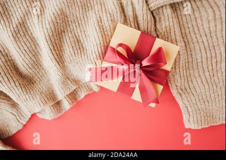 boîte beige avec ruban rouge satiné festif sur chandail beige. présentation des cadeaux, mise au point sélective Banque D'Images