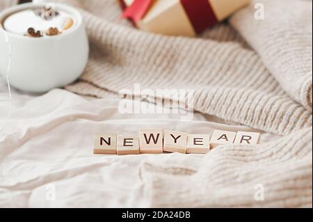 inscription nouvel an sur tissu beige froissé, boîte cadeau avec ruban rouge, guirlandes sur chandail beige tricoté sur fond. carte du nouvel an confortable et festif, s Banque D'Images