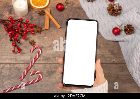 mockup téléphone portable sur fond de table en bois pendant les vacances de Noël. Femme tient un téléphone portable avec un écran blanc vierge. Vue de dessus. Gros plan Banque D'Images
