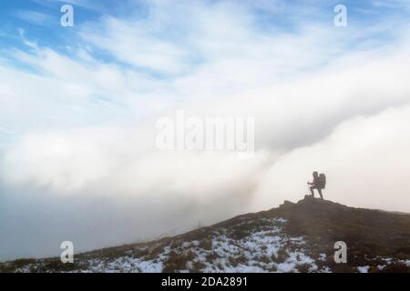 Randonneur debout sur le sommet de la montagne devant dramatique nuages et vent fort Banque D'Images