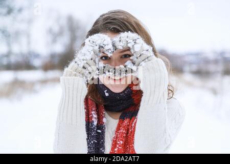 Une jeune fille heureuse dans un foulard tricoté rouge et des moufles blanches. Banque D'Images