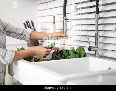 Les mains de femme lavent la laitue dans l'évier de cuisine de près. Banque D'Images