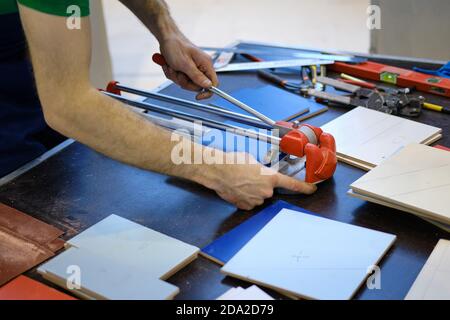 Les hommes coupent les matériaux de construction sur une table avec un coupe-carreaux manuel Banque D'Images