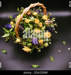 Beau bouquet de roses sèches jaunes et bleues. Fleurs dans un panier en osier sur fond noir. Composition des fleurs flétrissent. Violet et jaune r Banque D'Images