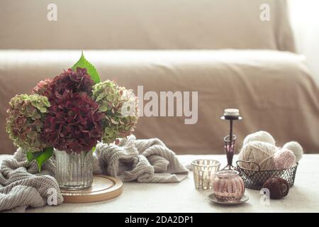 Encore la vie avec un bouquet d'hortensia, un pull chaud, des fils et des petites choses décoratives pour la maison sur un fond flou. Banque D'Images