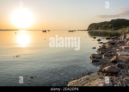 Magnifique lever de soleil sur la baie paisible de la mer Baltique avec petits bateaux et rivage rocheux Banque D'Images