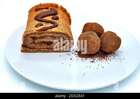 Pâtisseries maison parsemée de cacao. Un rouleau de beurre avec des boules de chocolat sur une grande assiette. Rouleau de chocolat fait à la main, isoler sur fond blanc. Banque D'Images